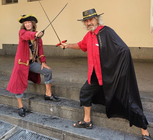 Zwei kostümierte Männer führen einen Degenduell-Kampf auf einer Treppe auf: einer als Pirat verkleidet, der andere als Zorro mit schwarzem Umhang und Hut mit dem Buchstaben Z.